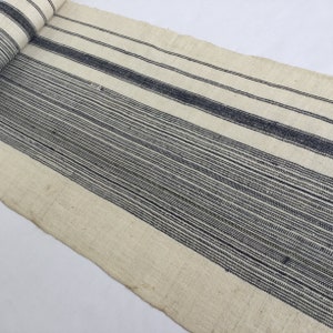 May include: A white fabric with black stripes woven into the material. The stripes are of varying widths and some are very thin.