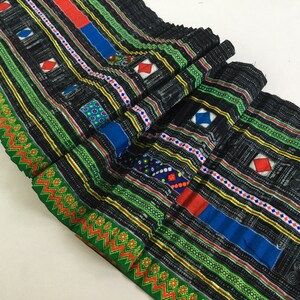 May include: Black fabric with colorful stripes and geometric patterns. The fabric has a woven texture and is decorated with red, blue, green, and white accents.