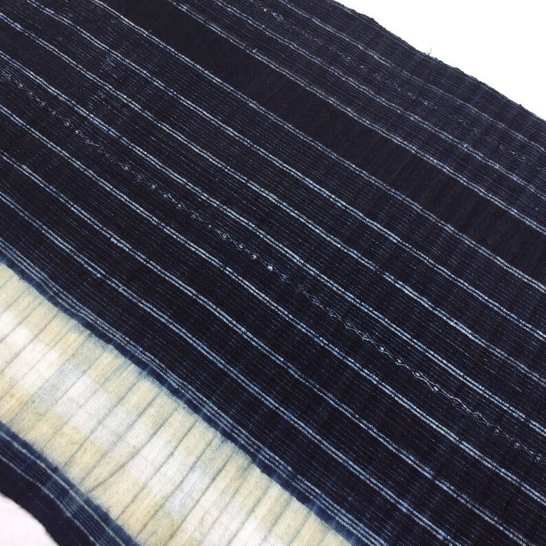 May include: A close-up of a blue and white striped fabric with a white border. The fabric has a textured, woven appearance.