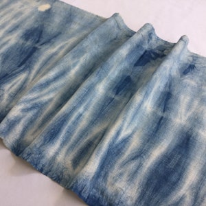 Op de afbeelding: Een close-up van een blauwe en witte tie-dye stof. De stof is gevouwen en heeft een zachte, textuur.