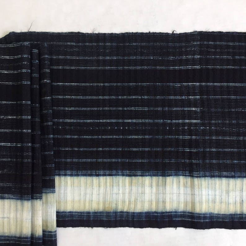 May include: Black and white striped fabric with a white and blue stripe at the bottom. The fabric has a textured, woven look.