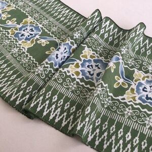 Könnte beinhalten: Grüner Stoff mit einem weißen Blumenmuster. Der Stoff hat ein sich wiederholendes Muster aus Blumen und Blättern. Der Stoff ist in der Mitte gefaltet.