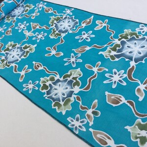 Könnte beinhalten: Ein türkisfarbener Stoff mit einem weißen und braunen Blumenmuster. Der Stoff hat ein dezentes Batik-Design mit einem sich wiederholenden Muster aus Blumen und Blättern.