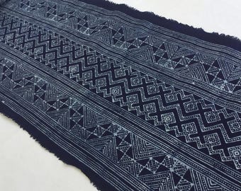 May include: A close-up of a dark blue fabric with a white geometric pattern. The fabric has a frayed edge and is woven with a traditional design.