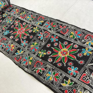 May include: Black fabric trim with colorful embroidered floral and geometric patterns. The trim features silver thread and a variety of colors including red, green, yellow, and blue.