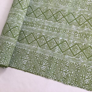 Pu&ograve; includere: Tessuto verde e bianco con un motivo geometrico. Il tessuto &egrave; arrotolato e ha un bordo sfilacciato.