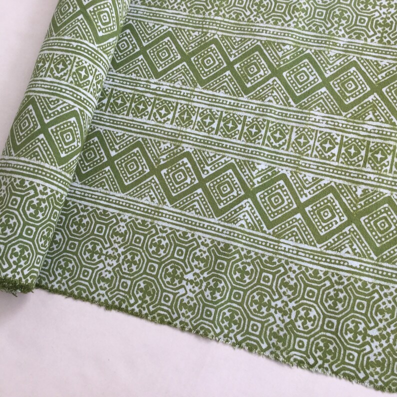 Pu&ograve; includere: Tessuto verde e bianco con un motivo geometrico. Il tessuto &egrave; arrotolato e ha un bordo sfilacciato.