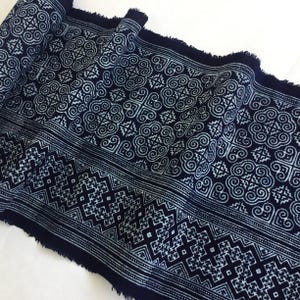 May include: A close-up of a dark blue fabric with a white geometric pattern. The fabric is folded and has a frayed edge.