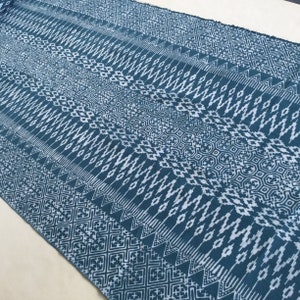 Könnte beinhalten: Tealfarbener Stoff mit einem weißen geometrischen Muster. Das Muster besteht aus sich wiederholenden Formen, darunter Rauten, Quadrate und Dreiecke.