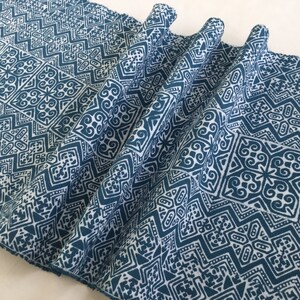 Könnte beinhalten: Ein Nahaufnahme eines blaugrünen Stoffes mit einem weißen geometrischen Muster. Der Stoff ist gefaltet und hat eine strukturierte Oberfläche.