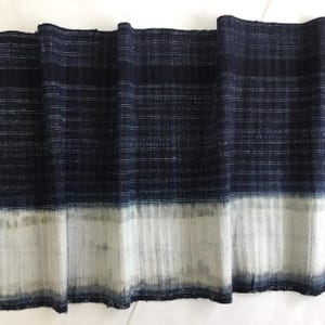 May include: A folded textile with a dark blue and white striped pattern. The fabric has a faded, distressed appearance, with a lighter, almost bleached, white section at the bottom. The textile appears to be handmade.