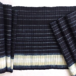 May include: A close-up of a dark blue and white striped fabric with a white border. The fabric is folded in half and has a textured surface.