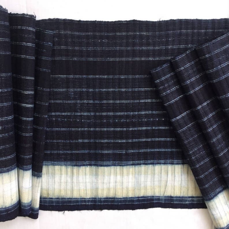 May include: A close-up of a dark blue and white striped fabric with a white border. The fabric is folded in half and has a textured surface.