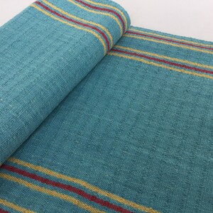May include: A teal blue woven rug with yellow and red stripes. The rug is folded in half, showing the texture of the weave.