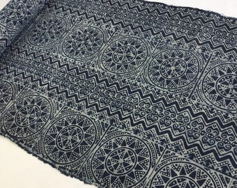May include: A close-up of a blue and white fabric with a repeating pattern of geometric shapes and circles. The fabric has a rough, textured surface.
