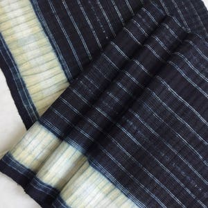 May include: A close-up of a blue and white striped fabric with a subtle texture. The fabric is folded and has a light blue border.