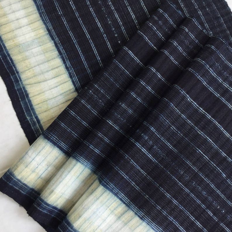 May include: A close-up of a blue and white striped fabric with a subtle texture. The fabric is folded and has a light blue border.