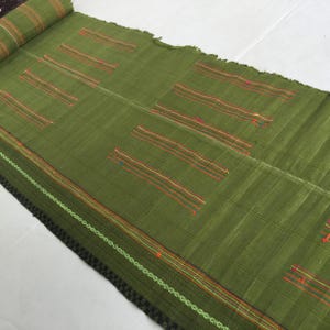 May include: A green woven rug with colorful stripes. The rug has a fringed edge and is made of a natural fiber.