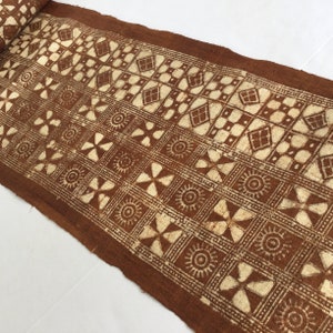 May include: A brown fabric with a white geometric pattern. The pattern includes squares, diamonds, and circles. The fabric is woven and has a rough texture.