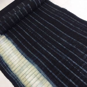 May include: A close-up of a dark blue fabric with white stripes. The fabric has a faded, light blue area at the bottom.