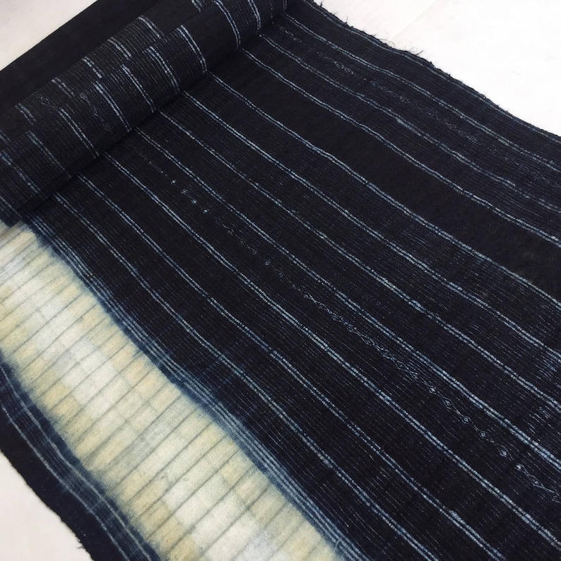May include: A close-up of a dark blue fabric with white stripes. The fabric has a faded, light blue area at the bottom.