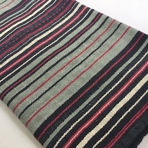 May include: Black, cream, and red striped woven throw blanket. The blanket is made of a soft, textured fabric.