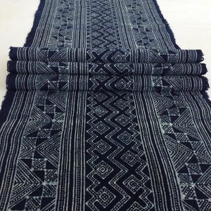 May include: A close-up of indigo blue fabric with a white geometric pattern. The fabric is folded in thirds and has a rough, textured surface.