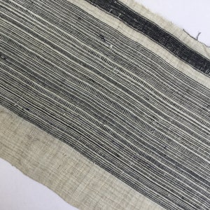 May include: A close-up of a woven fabric with a black and white striped pattern. The fabric has a rough texture and a natural, rustic look.