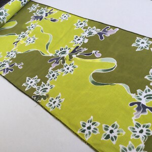 Könnte beinhalten: Ein grüner und weißer Stoff mit einem Blumenmuster. Der Stoff hat einen grünen Hintergrund mit weißen Blumen und einem dunkelgrünen und violetten Wirbelmuster.