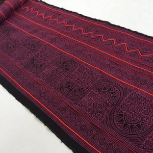 Könnte beinhalten: Schwarzer Stoff mit einem sich wiederholenden geometrischen Muster in Rosa- und Rottönen. Das Muster zeigt eine Reihe von geschwungenen Linien und geometrischen Formen.