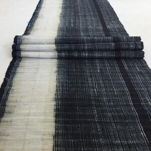 May include: A long piece of indigo dyed fabric with a white stripe down the center. The fabric is folded in thirds and has a rough, textured surface.