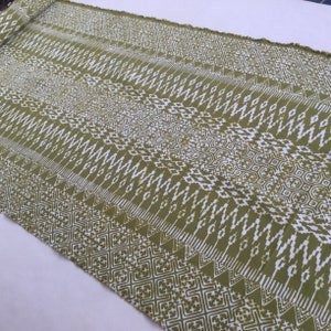 Könnte beinhalten: Grüner Stoff mit einem weißen geometrischen Muster. Der Stoff hat eine gewebte Textur und einen Fransenrand.
