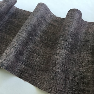 May include: A close-up of a dark brown fabric with a textured weave. The fabric is folded and has a slightly rough surface.