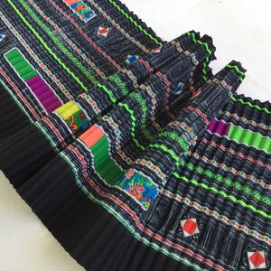 May include: Black fabric with colorful embroidered patterns. The fabric is pleated and has a geometric design. The colors include green, red, orange, yellow, purple, and blue.