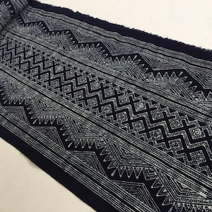 Puede incluir: Tela índigo con un patrón geométrico blanco. El diseño incluye zigzags, diamantes y líneas. La tela tiene un borde crudo y deshilachado. Ideal para confección de ropa o decoración del hogar.