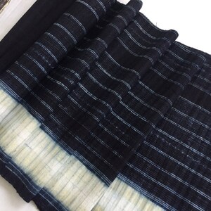 May include: A close-up of a black and white striped fabric with a white border. The fabric is folded and has a textured surface.