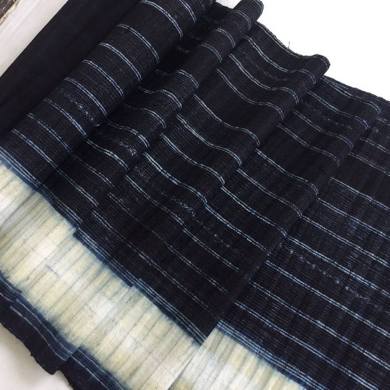 May include: A close-up of a black and white striped fabric with a white border. The fabric is folded and has a textured surface.