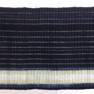 May include: A close-up of a dark blue fabric with white stripes. The fabric has a textured, woven appearance and a white border at the bottom.
