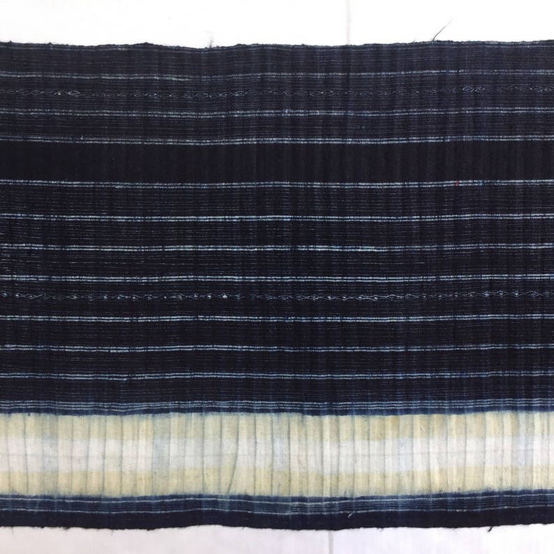 May include: A close-up of a dark blue fabric with white stripes. The fabric has a textured, woven appearance and a white border at the bottom.