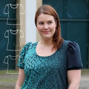 Könnte beinhalten: Ein kurzärmliges Oberteil in Teal und Marineblau mit floralem Muster. Das Oberteil hat einen Rundhalsausschnitt und dunkelblaue Ärmel. Das Design zeigt eine große, stilisierte Blume in Teal- und Marineblautönen. Das Oberteil wird mit einer blauen Jeans kombiniert.