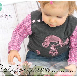 Puede incluir: Un bebé con una camisa de manga larga rosa y gris con un gráfico de una niña en la parte delantera. La camisa tiene una manga con estampado rosa y blanco. El texto "...Baby longsleeve..." está en la parte inferior de la imagen.