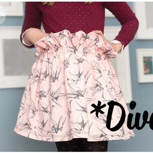 Könnte beinhalten: Ein rosa Rock mit einem schwarzen und weißen Origami-Vogel-Druck. Der Rock hat einen gerafften Bund und wird von einem Kind getragen. Der Text *Diva* ist in schwarz unten rechts im Bild geschrieben.