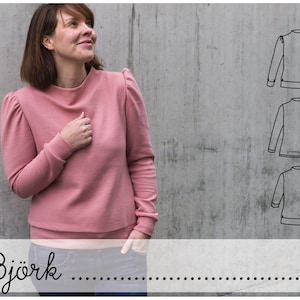 Könnte beinhalten: Ein rosa Pullover mit Puffärmeln und einem hohen Ausschnitt. Der Pullover wird an einem Modell gezeigt und auch als Strichzeichnung in drei verschiedenen Ansichten.