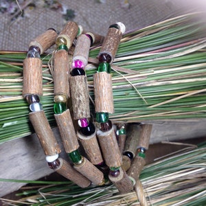 May include: A multi-strand bracelet made of natural wood beads and colorful glass beads. The bracelet is wrapped around a bundle of dried grass.