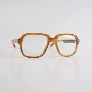 May include: A pair of vintage eyeglasses with a light brown, square frame. The lenses are clear, and the frame has a subtle marbled effect. The glasses have a classic, retro style.