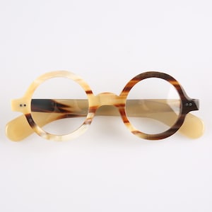 May include: Round eyeglasses with a two-tone frame in shades of tan and brown. The glasses have a keyhole bridge and clear lenses. The temples and earpieces are a solid tan color. The glasses are set against a white background.