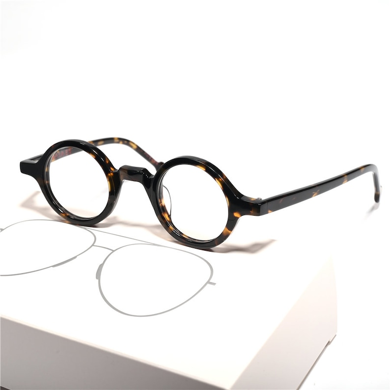 Pu&ograve; includere: Occhiali rotondi in tartaruga con lenti trasparenti. Gli occhiali hanno uno stile classico e vintage.