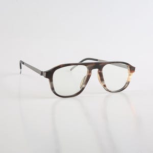 May include: Spectacles featuring a brown and tan tortoiseshell pattern on the frame front with a distinct top bar bridge. The temples are thin and dark grey, connecting to the frame with a hinge. The lenses are clear and transparent.