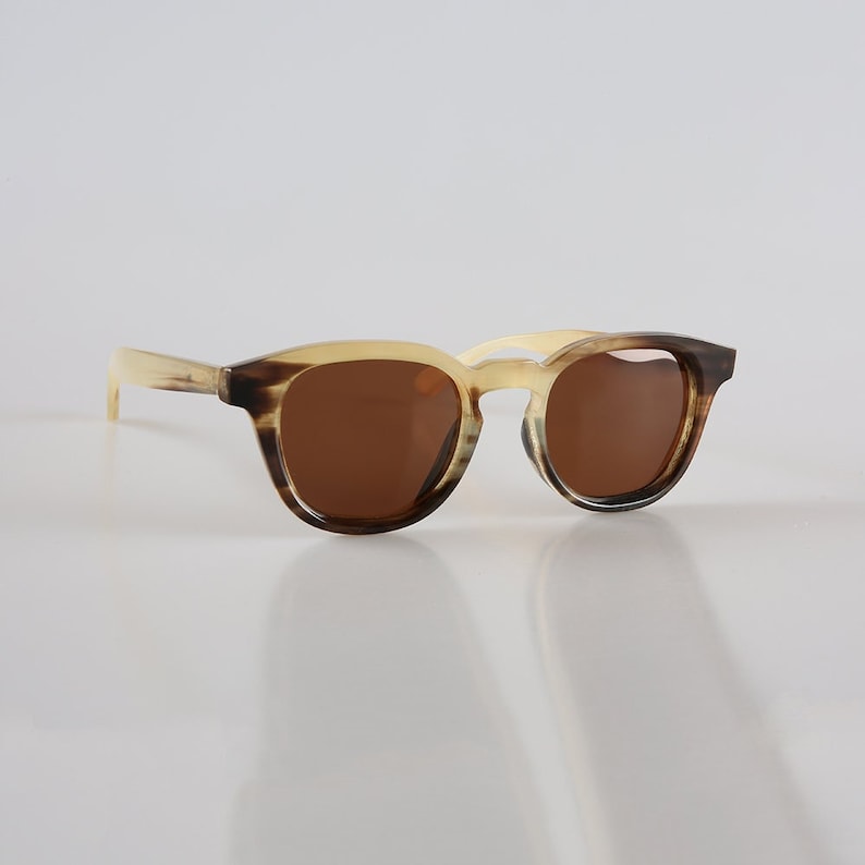 May include: Tortoiseshell sunglasses with brown lenses. The frame is a light brown colour with a darker brown pattern.