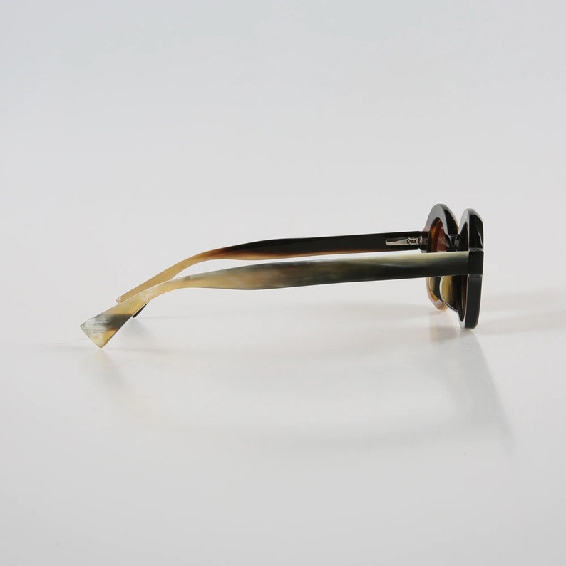 May include: A pair of horn-rimmed sunglasses with a dark brown frame and light brown temples. The sunglasses have a rounded shape and are made of a natural material.